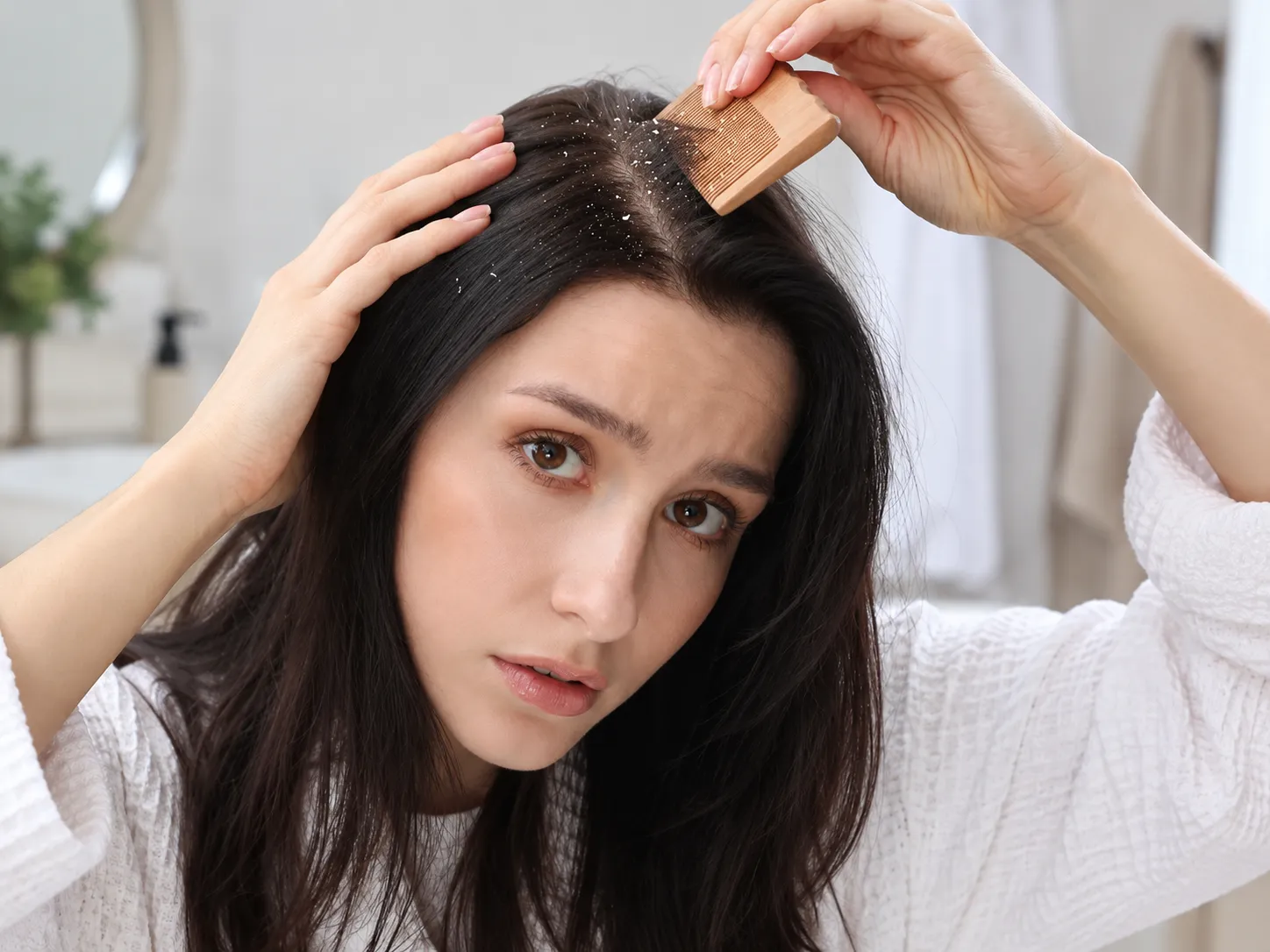 Woman examining visible dandruff flakes along her scalp using a wooden comb